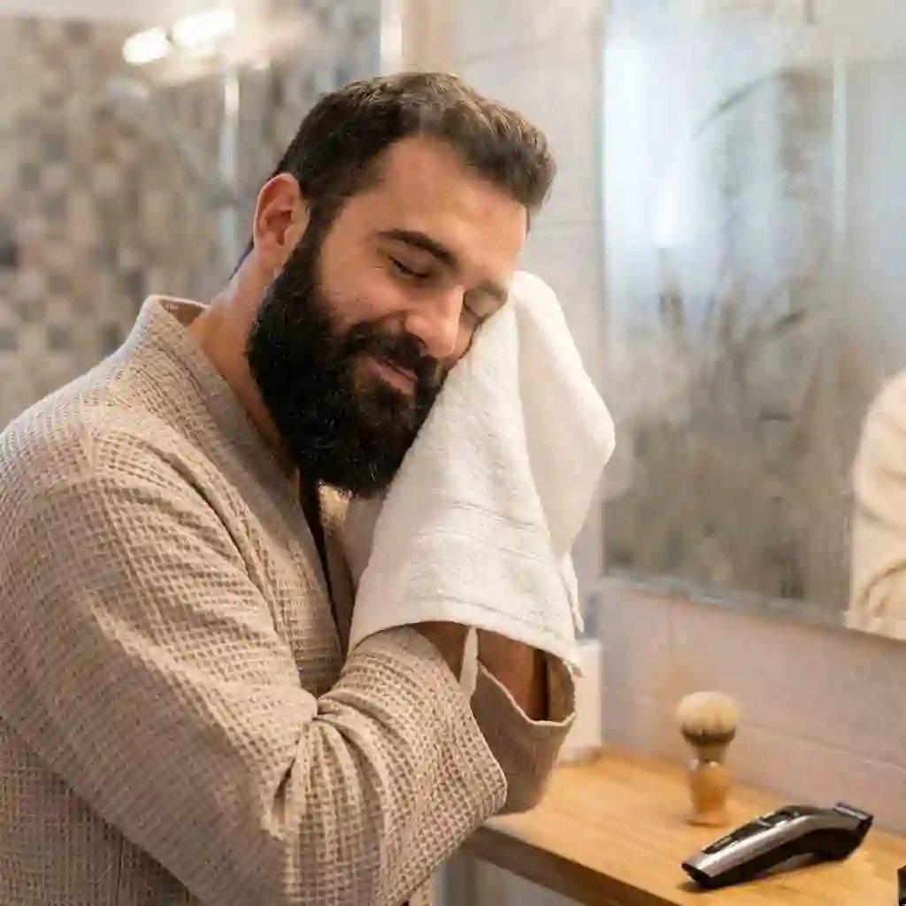 Man washing his face with warm water and beard shampoo to prepare his facial hair for trimming with a beard shaper, ensuring a smooth and comfortable grooming experience.