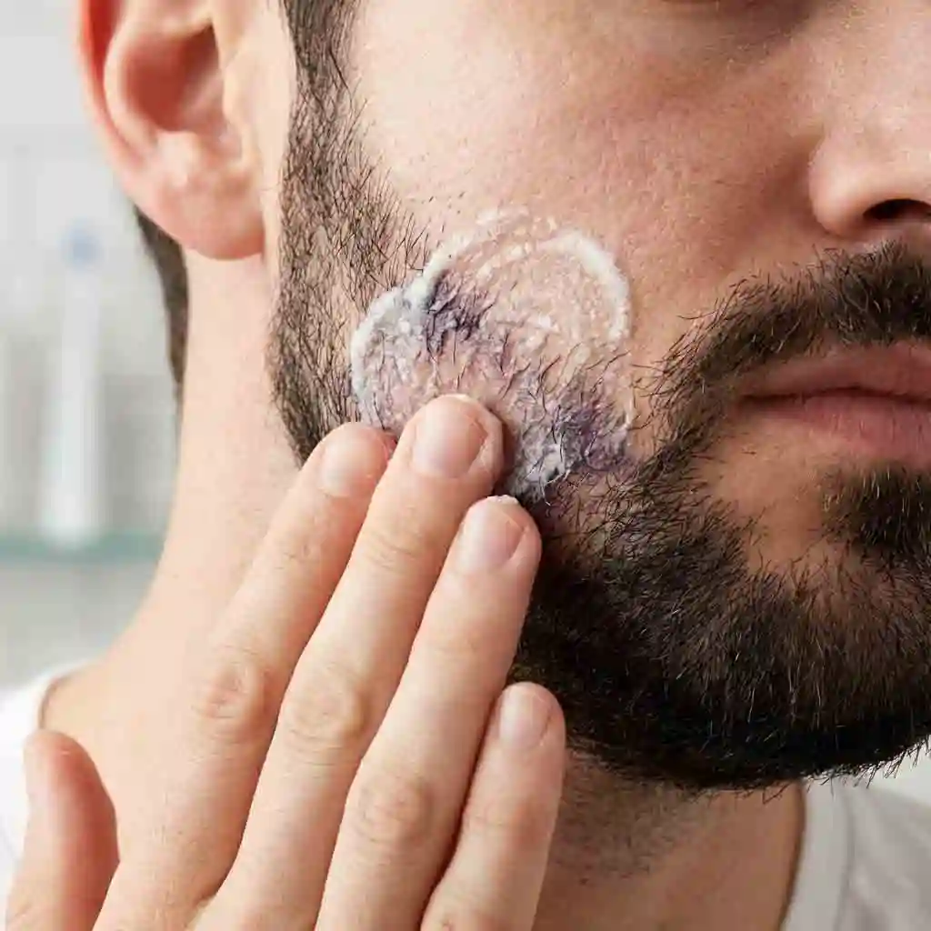A man gently applying a baking soda and dish soap paste to his cheek, following the steps on how to remove beard dye from facial skin.