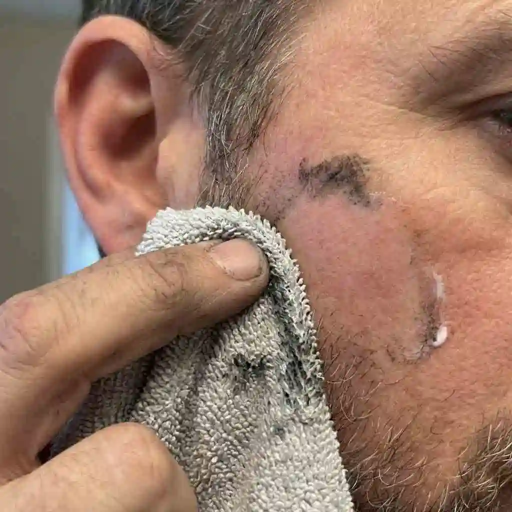 Wiping away the toothpaste with a damp cloth to reveal clear skin, proving this method works for how to remove beard dye stains along the hairline.